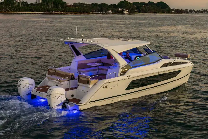 A sleek white motor yacht with blue LED lights navigates calm waters at sunset, showcasing luxurious seating and design.